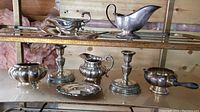 Full set view of silver plated candlesticks, creamers, sugar bowl, gravy boat and tray placed on glass shelf