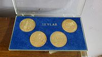 Four Skylab commemorative coins in blue velvet-lined display case with clear plastic lid, showing arrangement and storage.