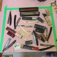 Full set of vintage straight edge razors, sharpening stones, and cases on a pink surface with green tape border.
