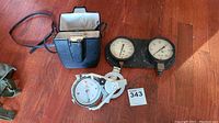 Photo of the full lot showing the surveying compass, its case, and the Fahrenheit gauge on wooden floor.