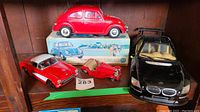 Three toy cars: Volkswagen Beetle on box, red 1957 Chevy Corvette with parts, black RC car