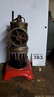 Front view of the toy steam engine showing brass flywheel and red base with ventilation cutouts