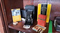 Overview of vintage Kodak camera, portrait attachment box, flashbulb boxes and negatives case on wooden shelf
