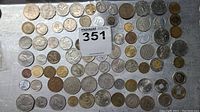 Photo showing an assortment of about 70 coins laid out on a metallic surface, various shapes, sizes, and colors visible.