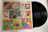 Photo showing the front cover with colorful comic strip artwork and the vinyl record partially out of its sleeve.