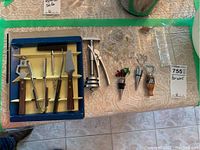 Blue and beige lined 5-piece bar opener set with various opener tools displayed alongside multiple wine stoppers of different designs and materials on lace tablecloth