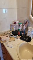Photo of various bathroom and beauty items on a countertop including boxed shower sole edge protector, curling iron, back belt, hair dryer, wood massager, and other small items.