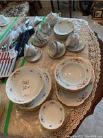 Wide view showing the full set of china dinnerware including plates, tea cups, saucers, and a bowl arranged on a table with lace tablecloth.