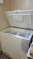 Closed white chest freezer with top lid open revealing divided interior with ice cube trays.