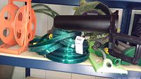 Orange plastic garden hose reel with circular reel and handle, coiled green hose sections, and garden watering accessories placed on a blue shelf.