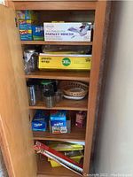 Photo of wooden shelf with various kitchen storage and prep items including boxes of Glad bags, Ziploc bags, plastic wrap, parsley mincer, jars, and foil.