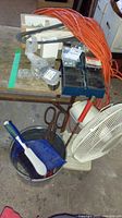 Overview of the lot showing extension cord, tin snips, fan, dustpan and brush, scissors on wooden table in garage