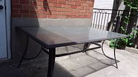 Full view of rectangular glass top patio table outdoors near brick wall and a small gate.