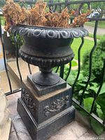 Side view of black cast iron urn-shaped planter on square pedestal base