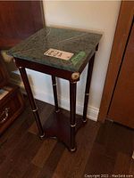 Front left angled view of planter stand showing stone top, wood legs with gold decorative accents and lower shelf.