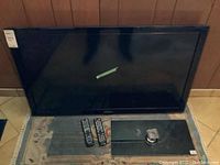 Black Samsung 46-inch LED TV on carpeted floor with two remote controls and glass stand.