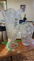 View of two crystal vases on a wooden surface: one tall Shannon Irish crystal vase marked 16-inch, and a shorter unmarked etched crystal vase.