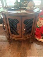 Wood side table showing curved front with two lattice inset doors, ornate feet, and wooden finish.
