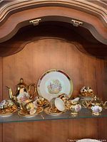Full display of porcelain Bavaria tea set including coffee pot, cups, saucers, creamer, sugar bowl, and plates on shelf with wood background.
