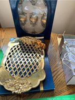 Royal Doulton brass trivet with floral design on top of its blue box and boxed set of six decorative glasses with gold detailing visible in the background.