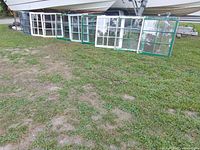 Ten windows leaning against a boat trailer on grass.