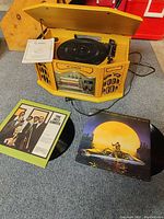 Full view of Curtis stereo featuring open lid showing turntable, two vinyl records on floor next to it with album covers, and manual on top.