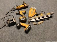 Lot of older Dewalt power tools including cordless drill, flashlight, corded reciprocating saw, cordless nail gun, charger, and batteries on carpeted floor.