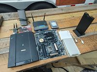 Photo showing all items in the lot including motherboard, router, scanner, hard drive, and docked external device