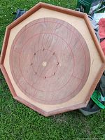 Octagonal wooden shuffleboard game board placed on grass showing concentric scoring rings and metal pegs, no pucks visible.