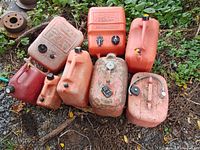 View showing all eight gasoline containers, arranged on the grass, highlighting varying sizes and conditions with some dirt and wear visible