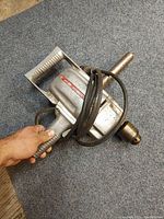 Heavy duty electric drill with handle and power cord wrapped around the body held in hand, showing overall size and condition.