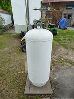 Front angled view of a large white cylindrical compressed air storage tank with pressure gauges and brass fittings on the top.