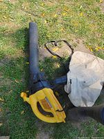 Photo showing the side view of the yellow and black leaf blower with the white collection bag attached, on grass surface.
