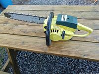 Side view of yellow Pioneer 1074 chainsaw on wooden table showing body, handle, and guide bar with chain.