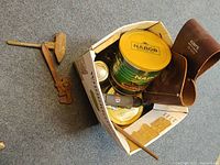 View of a box containing a wooden mallet, pipe wrench, leather tool pouch marked Klein Tools, rotary tool, and some tin containers.