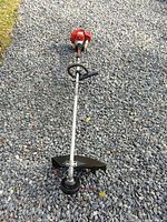 Full length view of the Shindaiwa T242x straight shaft trimmer showing the red engine, metal shaft, loop handle, and trimming head with protective guard.
