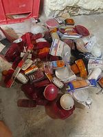 Pile of assorted trailer light lens covers and housings in red, white, amber colors laid out on floor.