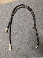 Three black rubber washer hoses laid on a gray carpeted surface, each with metal fittings on both ends, showing some wear and slight surface discoloration.