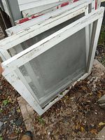 Three wooden framed window screens stacked outdoors showing white paint with chipping and grey mesh intact.