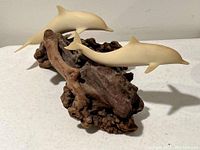 Side view of two light wooden dolphin figures attached to a textured natural wood base.