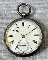 Front view of antique pocket watch showing white dial with black Roman numerals, two hands and small seconds subdial.