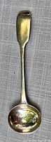 Full view of antique sterling silver spoon lying on grey fabric background.