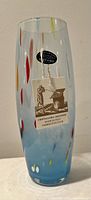 Tall cylindrical vase with multi color decoration and original tags attached, showing brand and origin.