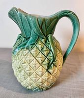 Front and side view showing the pineapple design with green leaves and handle, yellow textured body, and spout