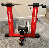 Front view of red Minoura Mag500 bicycle exercise adapter with adjustable axle clamps and resistance roller.
