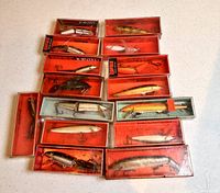 Top-down photo showing 15 Rapala fishing lures in original orange and blue boxes arranged on table.