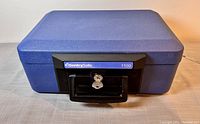 Front view of closed blue SentrySafe 1100 fire safe box with key in lock.