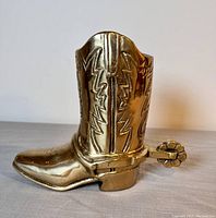 Side view of solid brass cowboy boot figurine showing detailed embossed stitching and attached spur.