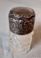 Side angle showing sterling silver embossed floral and scrollwork top with hallmarks and cut glass patterned bottle base.