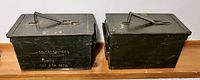 Photo showing two green vintage military metal ammunition boxes side by side on wooden surface.